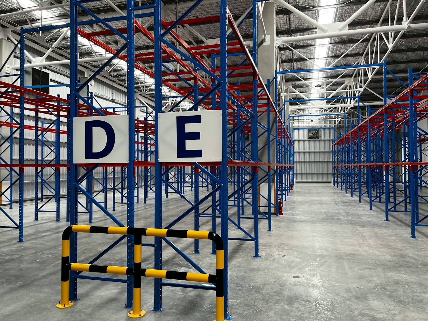 Almacén vacío con hileras de estanterías metálicas azules y rojas.